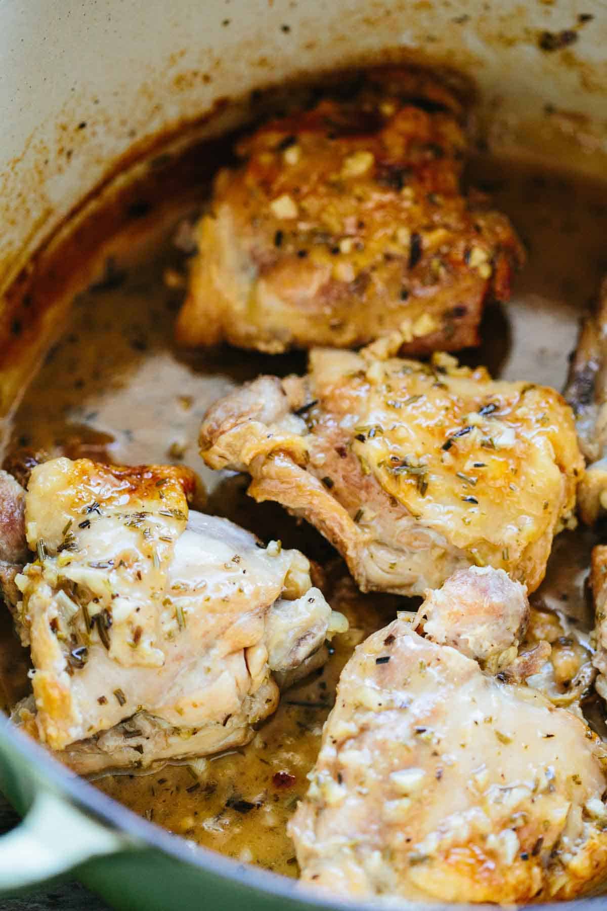 Interior view of a cooking pot or Dutch oven containing chicken thighs simmering in their sauce. This shows the cacciatore during its braising stage, with the chicken pieces glistening with herbs and aromatics in the flavorful cooking liquid.