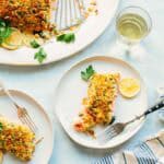 Elegant table setting featuring the breadcrumb-topped salmon served family style alongside individual portions. A glass of white wine complements the meal, with blue-striped napkins adding a coastal touch.