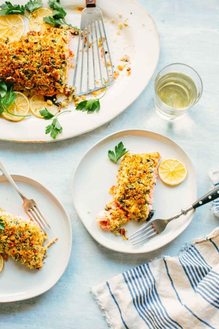 Elegant table setting featuring the breadcrumb-topped salmon served family style alongside individual portions. A glass of white wine complements the meal, with blue-striped napkins adding a coastal touch.