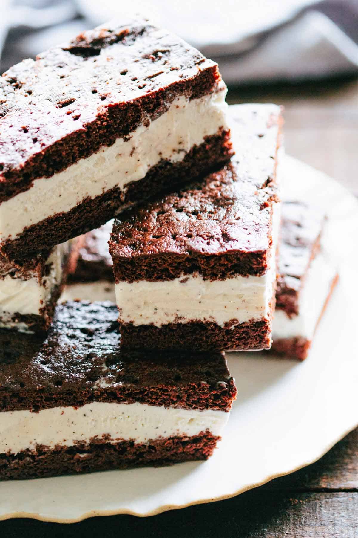 Stacked ice cream sandwiches on a white plate, showing neat layers of creamy vanilla ice cream between two thick, soft chocolate cookie slabs.