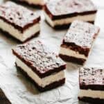 Multiple rectangular chocolate cookie ice cream sandwiches arranged on a sheet of crinkled white parchment paper, ready to serve or store.