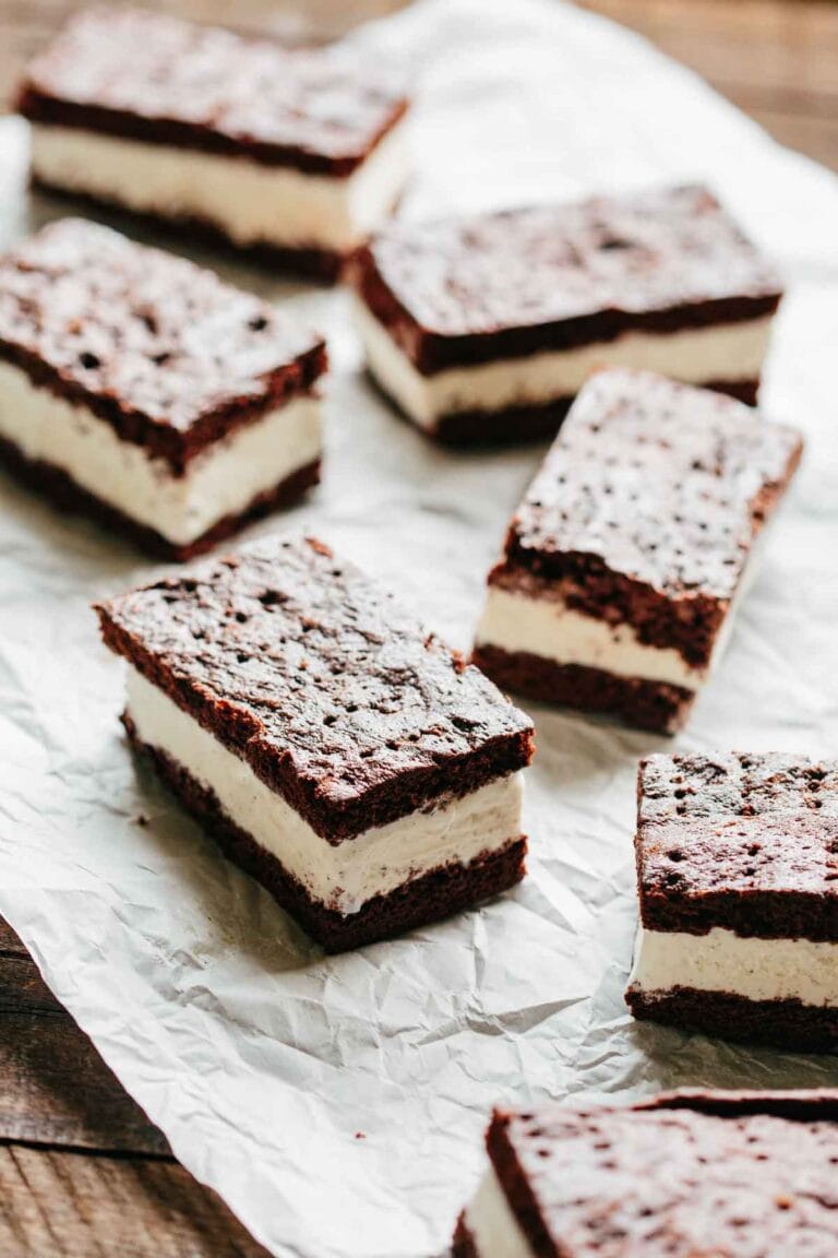 Multiple rectangular chocolate cookie ice cream sandwiches arranged on a sheet of crinkled white parchment paper, ready to serve or store.