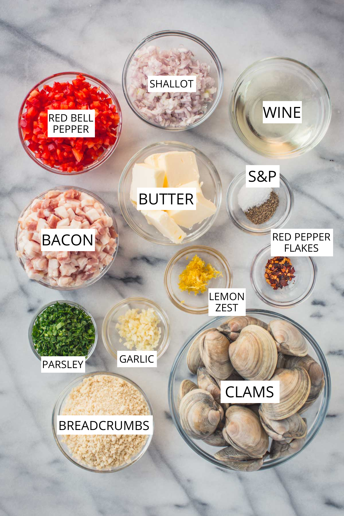 Labeled Clams Casino ingredients on marble:
Flat lay of ingredients including clams, bacon, breadcrumbs, red bell pepper, shallots, garlic, parsley, butter, lemon zest, wine, and seasonings.