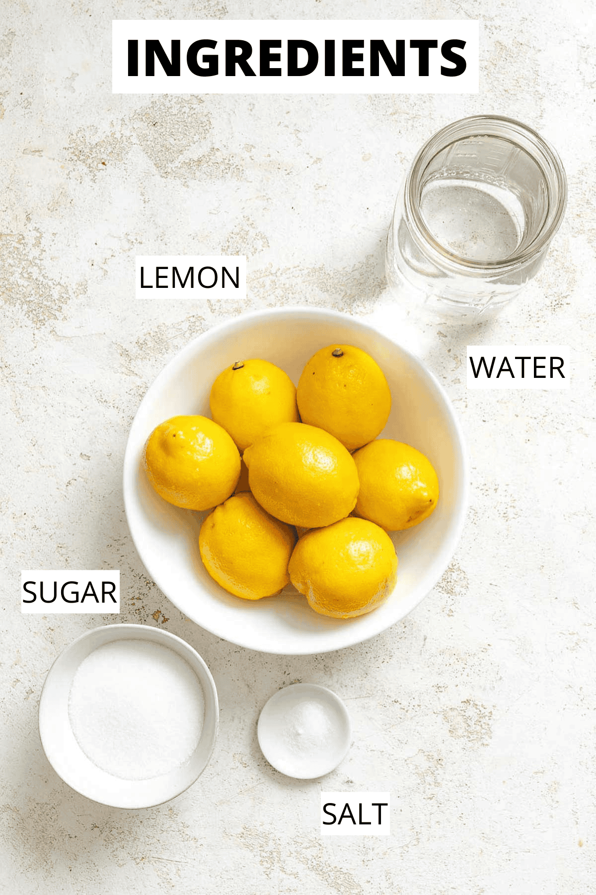 Overhead view of whole lemons, granulated sugar, and salt arranged on a countertop next to a mason jar of water—ingredients staged for making lemon granita.