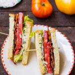 BLT sandwich cut in half and skewered, showing layers of bacon, tomato, lettuce, and mayo on white bread.