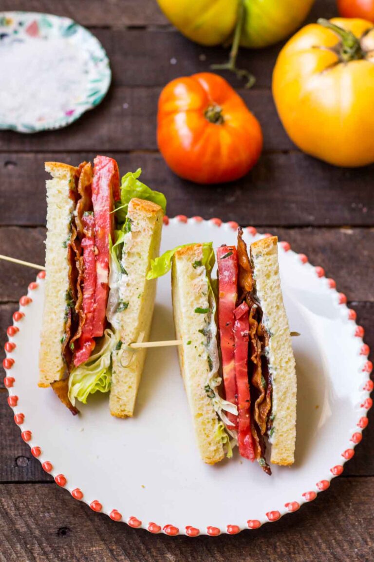 BLT sandwich cut in half and skewered, showing layers of bacon, tomato, lettuce, and mayo on white bread.