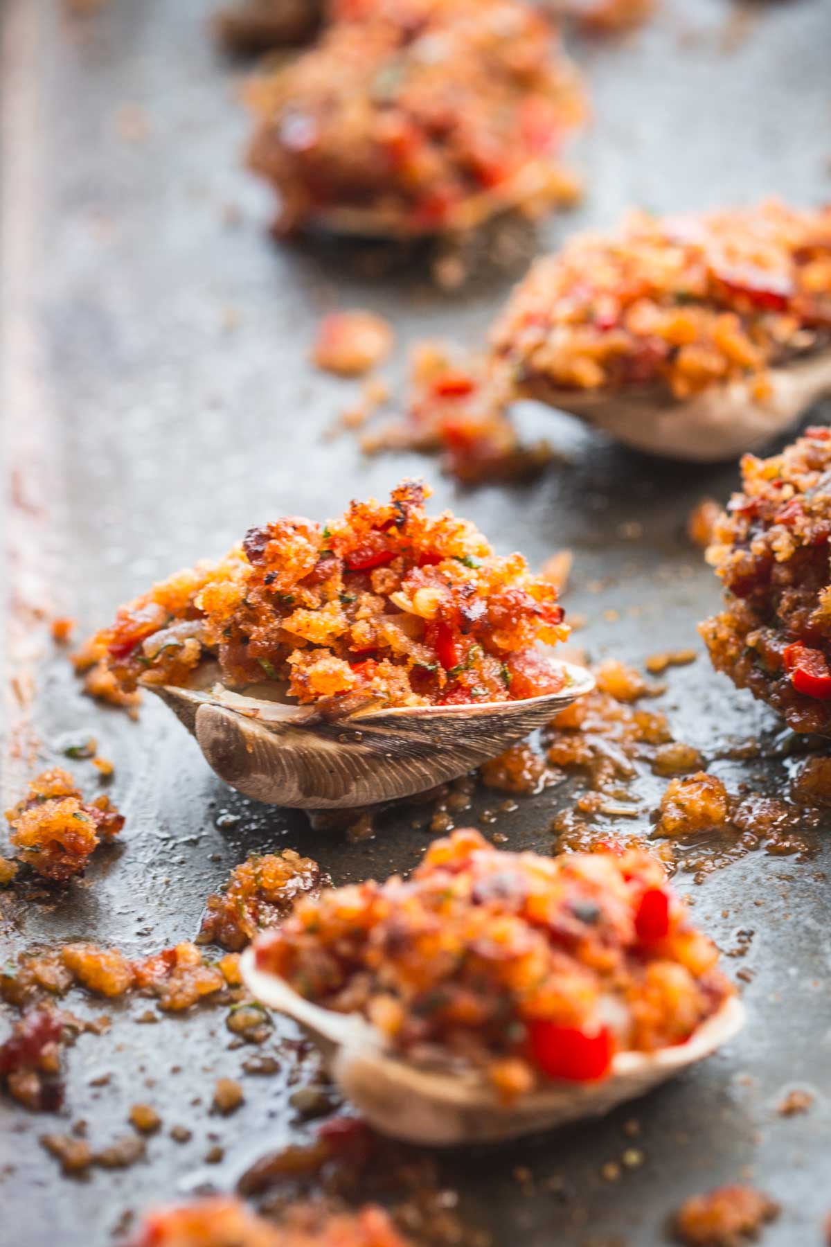 A baked clam stuffed with crispy breadcrumb topping and diced red peppers on a sheet pan.