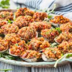 A large platter filled with Clams Casino arranged over arugula with a striped towel in the background.