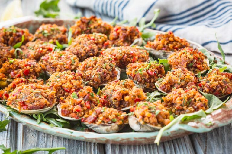 A large platter filled with Clams Casino arranged over arugula with a striped towel in the background.