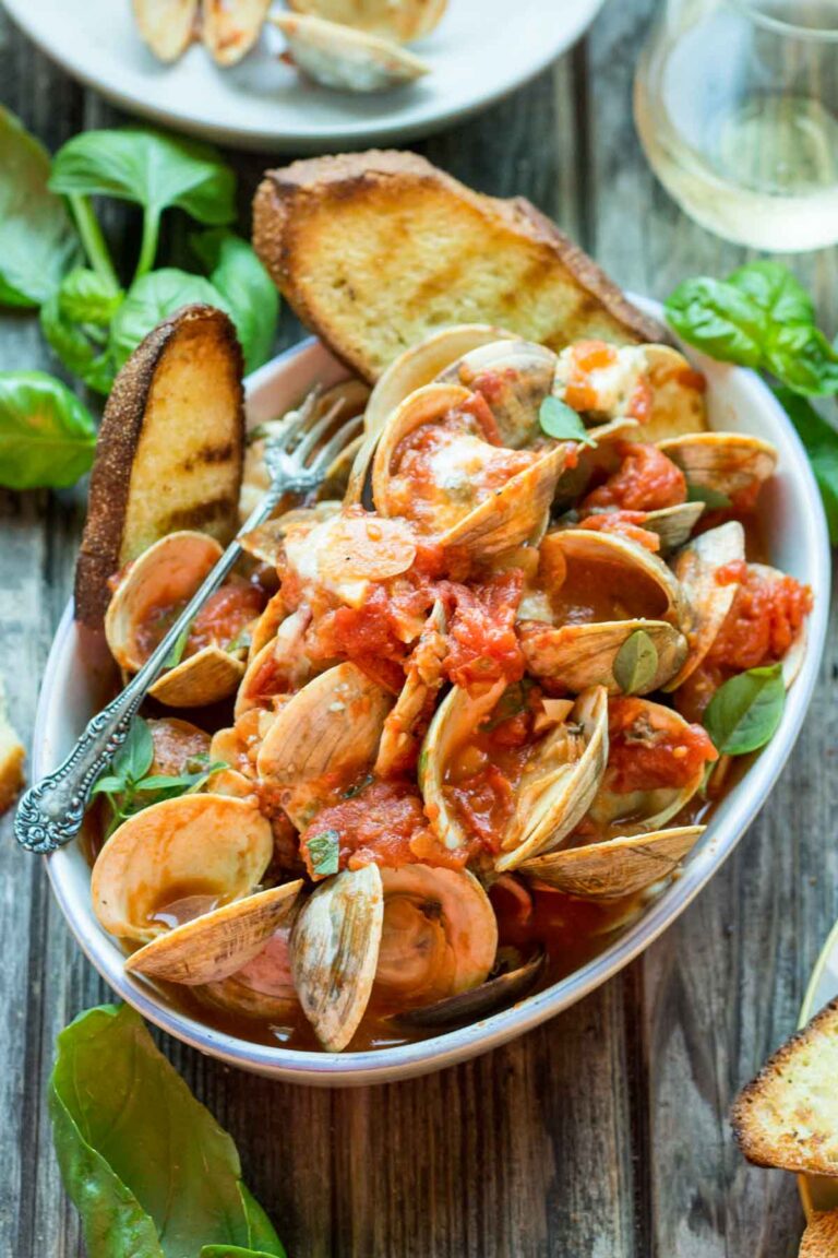Angled close-up of the main bowl, emphasizing the vibrant tomato sauce, opened clams, fresh herbs, and melted blue cheese, with a silver fork resting in the bowl.