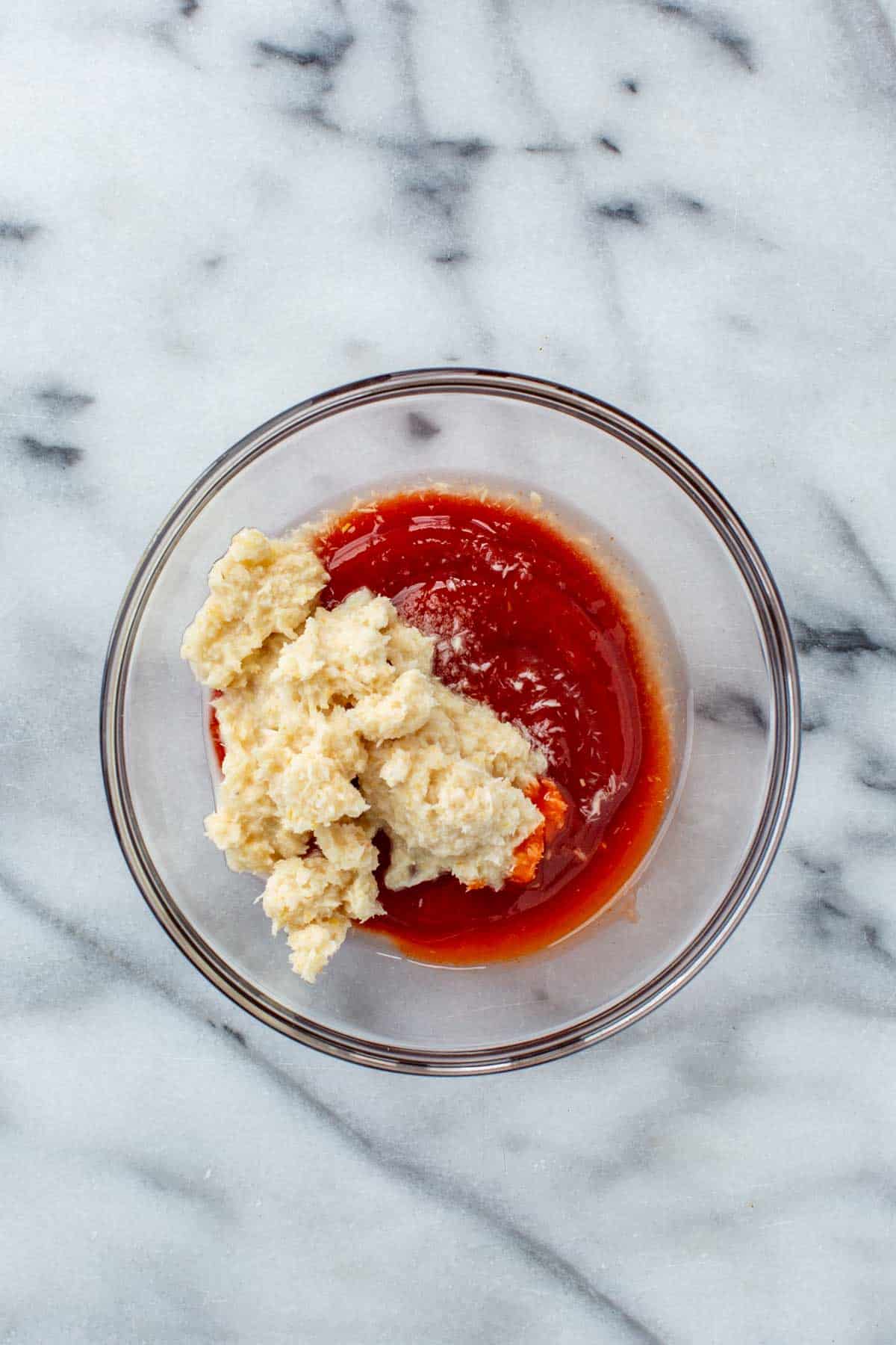 A glass bowl filled with ketchup, horseradish, hot sauce, lemon juice, and salt before being mixed together.