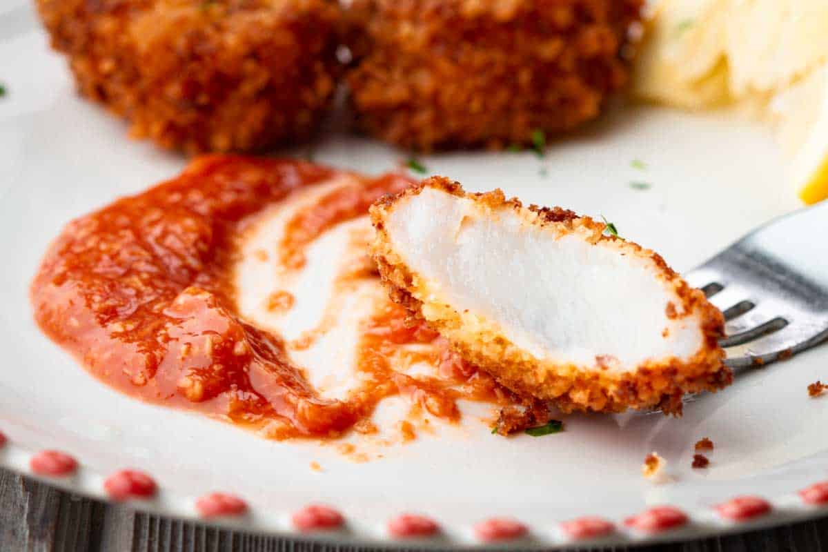 Crispy fried shrimp dipped into cocktail sauce on a white plate with red trim.