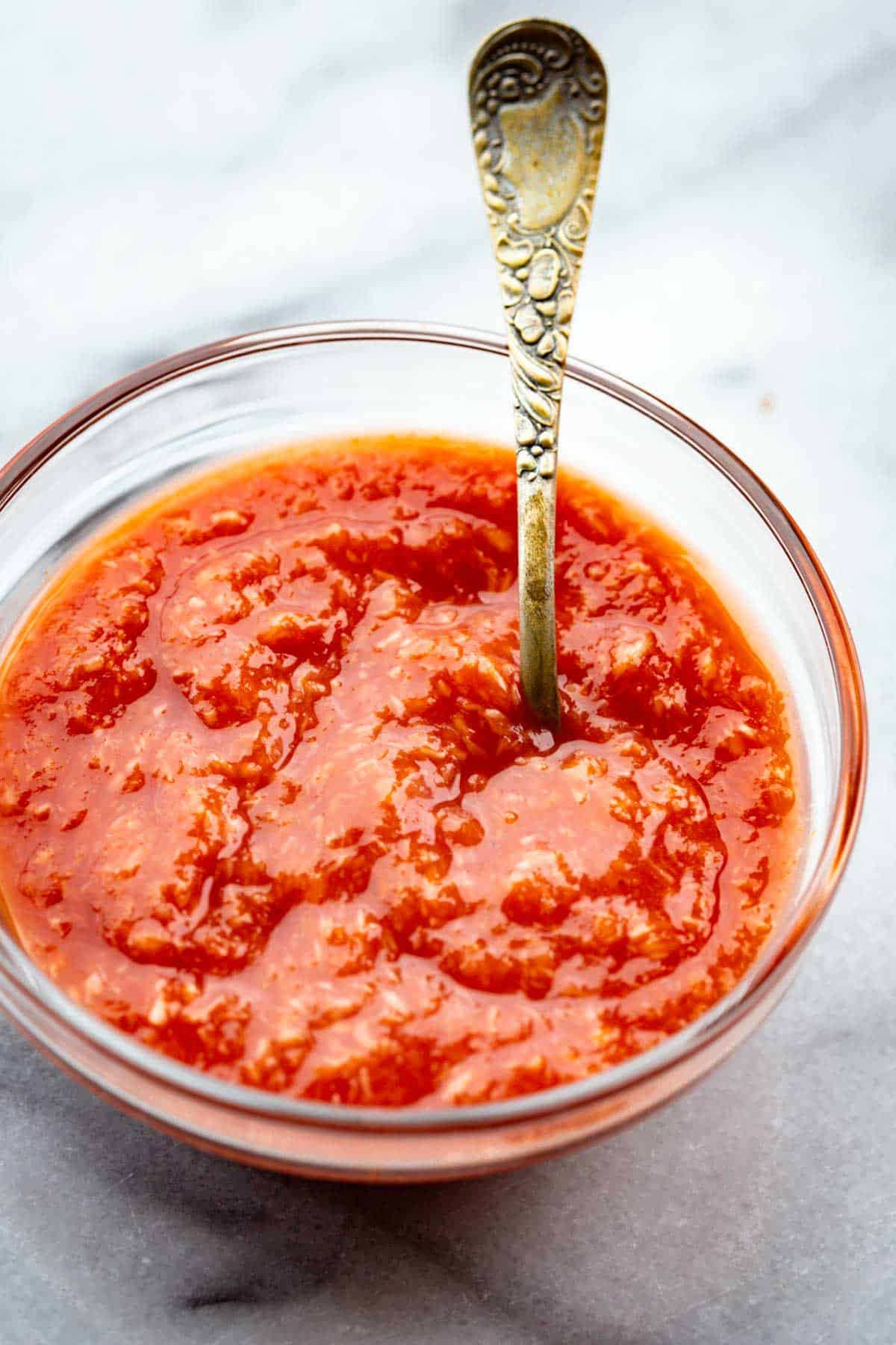 A close-up of cocktail sauce in a glass bowl with a vintage silver spoon resting inside.
