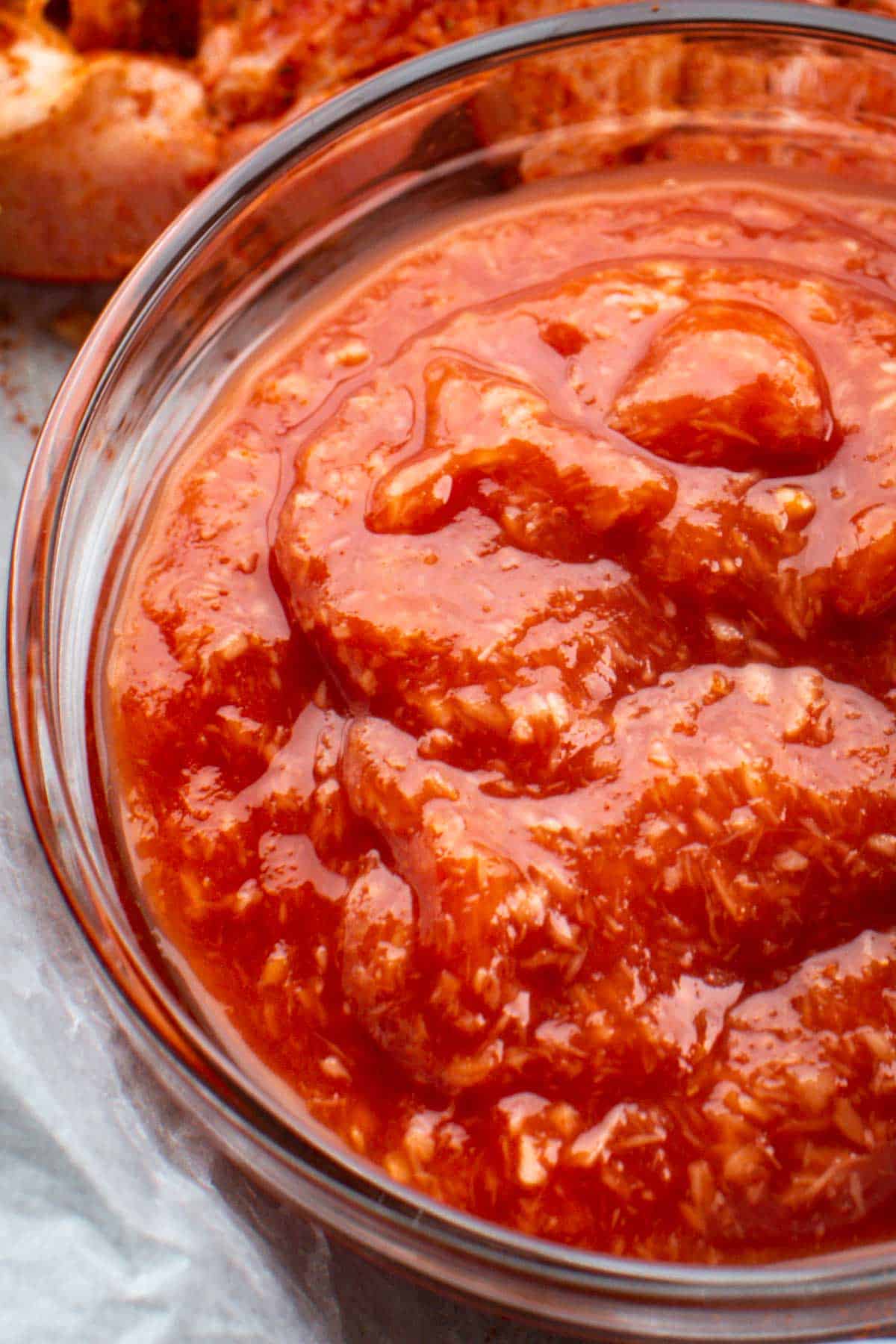 Macro view of thick, textured cocktail sauce in a clear glass bowl with visible flecks of horseradish.