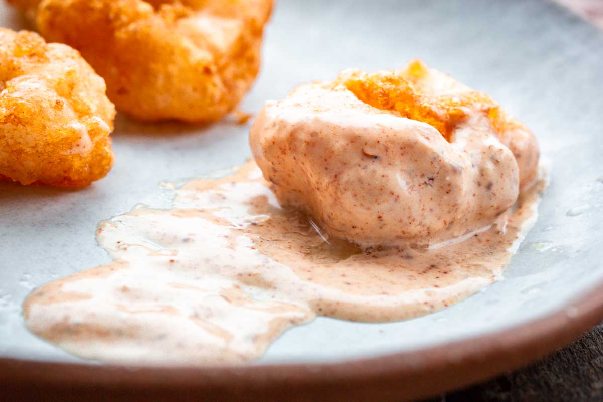 Close-up of a golden fried shrimp coated in thick Creole remoulade sauce on a ceramic plate.