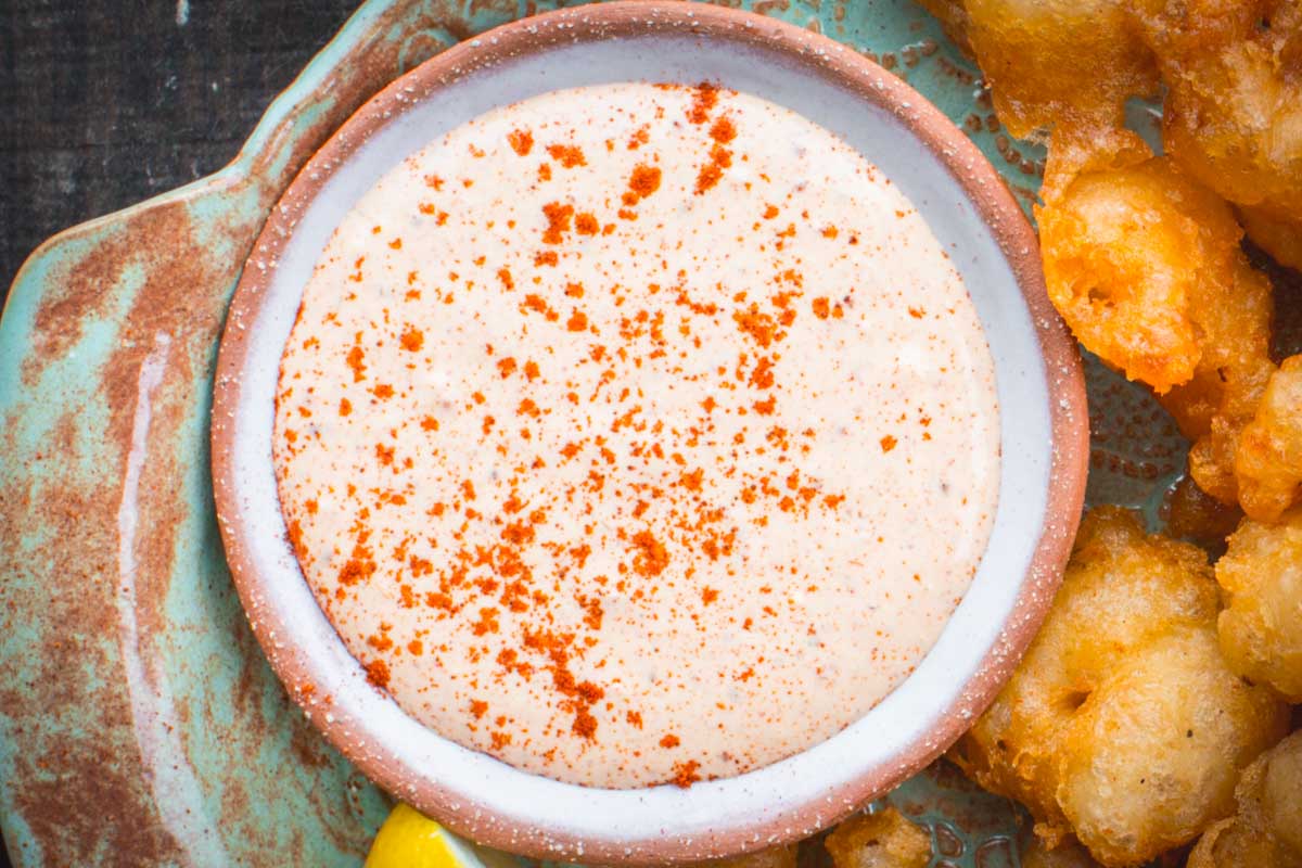 Overhead shot of a small ceramic bowl filled with Creole remoulade sauce, dusted with paprika and surrounded by crispy fried shrimp.