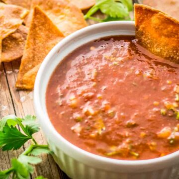 Close-up of salsa with chip dipped in: A white ramekin filled with tomato salsa, with a crispy tortilla chip dipped on the side.