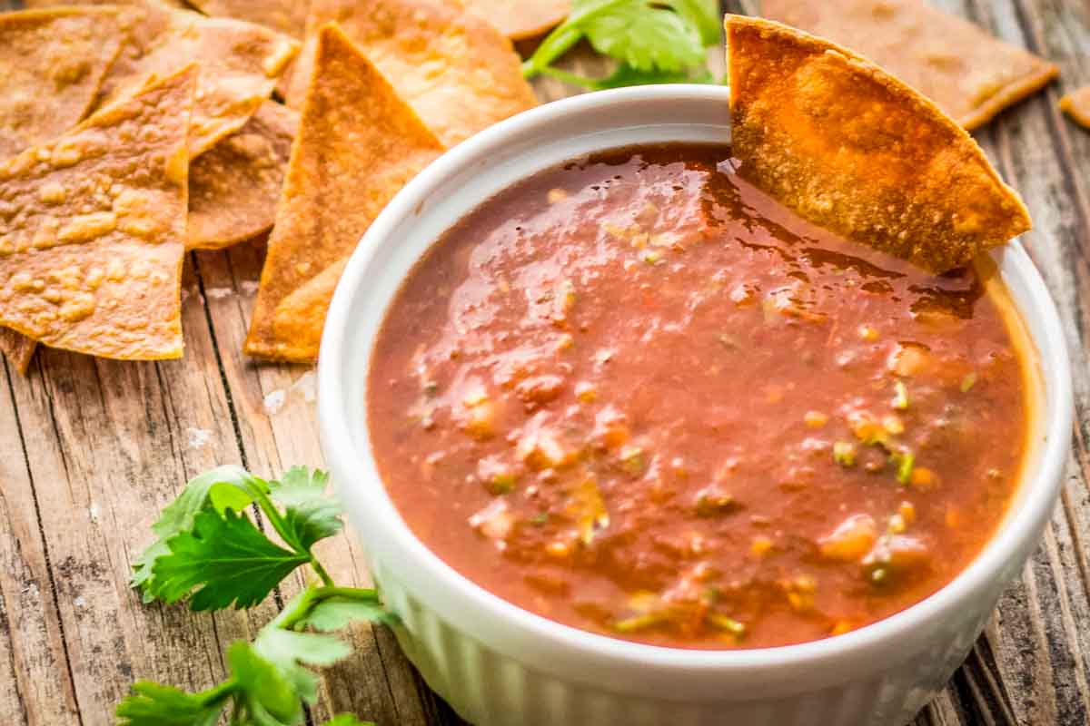Close-up of salsa with chip dipped in: A white ramekin filled with tomato salsa, with a crispy tortilla chip dipped on the side.