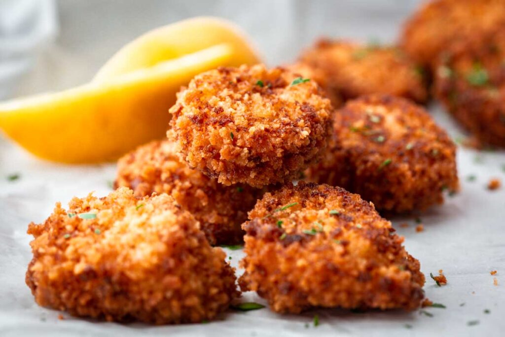 Close-up of fried scallops showing their crisp golden coating with lemon slices in the background.
