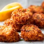 Close-up of fried scallops showing their crisp golden coating with lemon slices in the background.