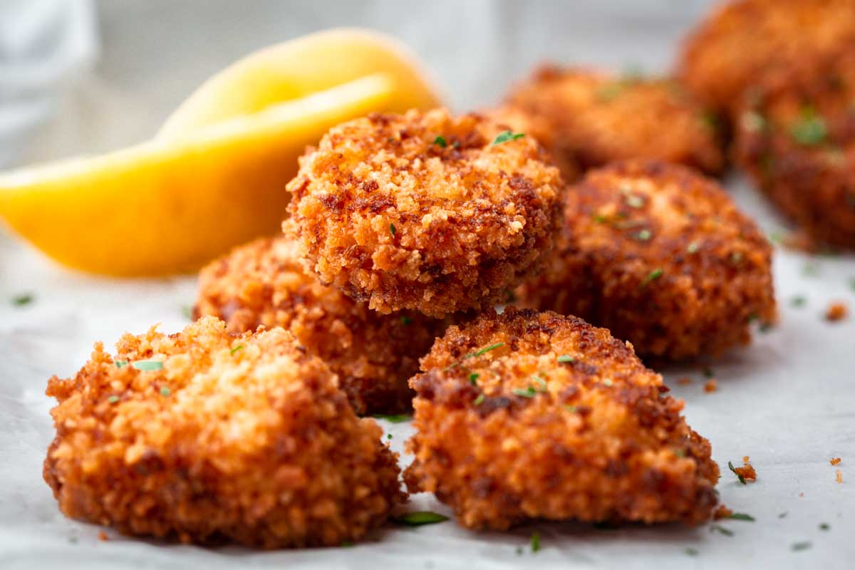 Close-up of fried scallops showing their crisp golden coating with lemon slices in the background.
