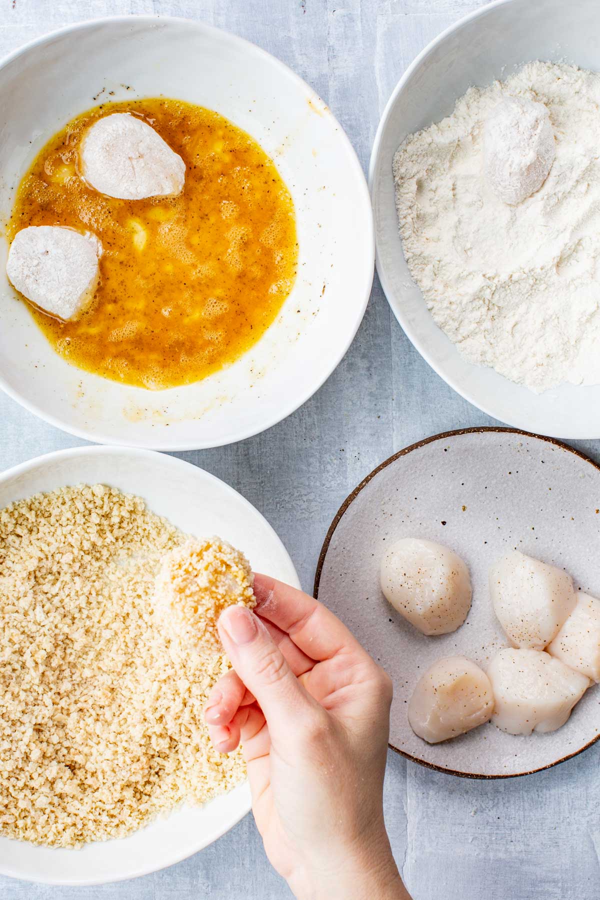 Action shot of breading scallops using flour, egg wash, and panko crumbs.