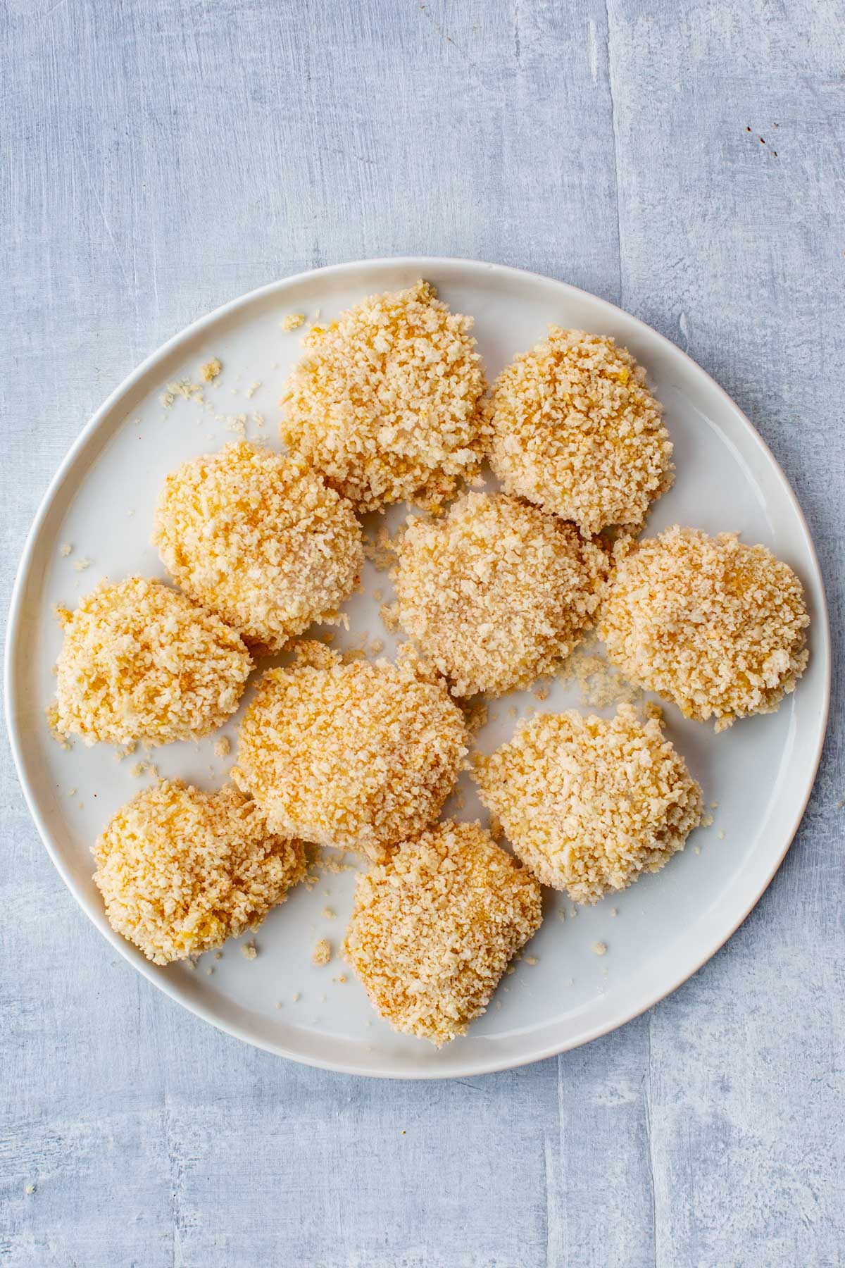 Plate full of scallops coated in a thick layer of panko breadcrumbs, ready to fry.