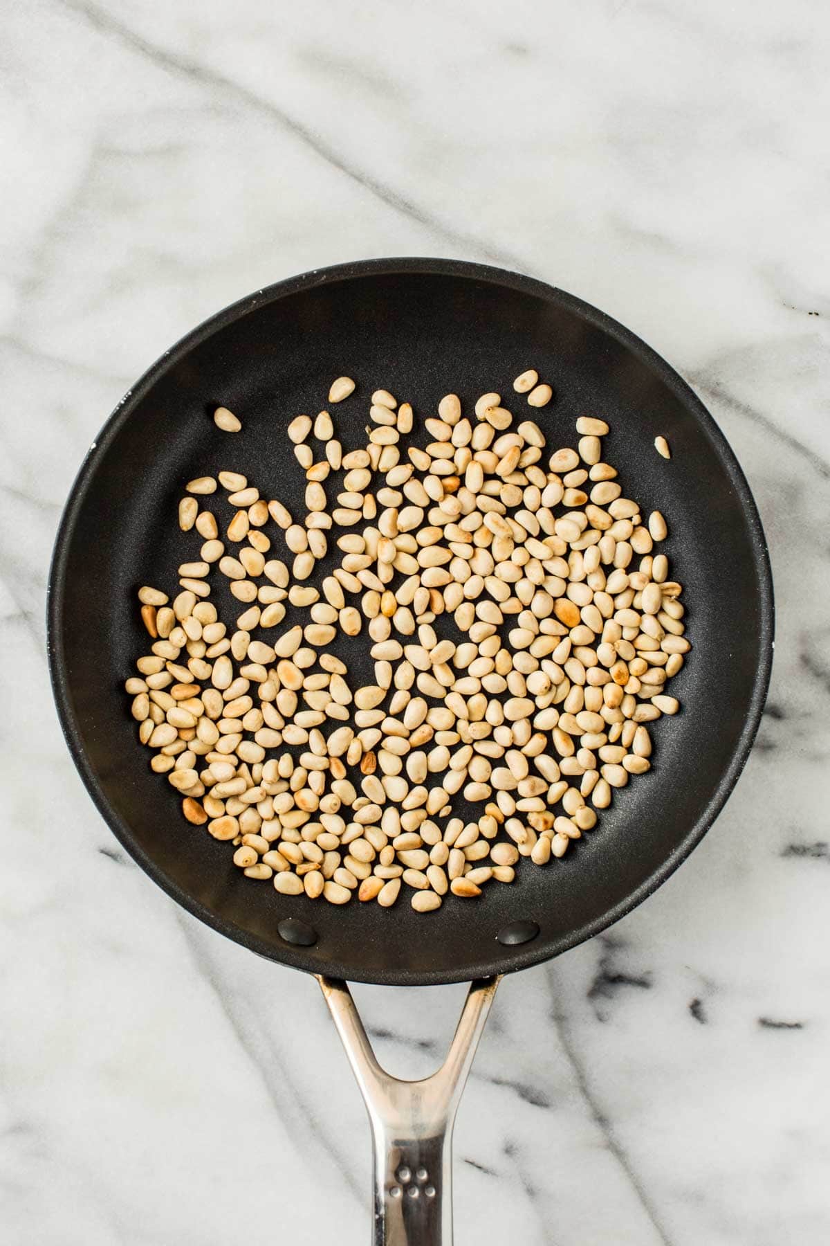 Flat-lay view of pine nuts being lightly toasted in a skillet to bring out their nutty aroma.