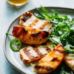 Grilled peaches and halloumi nestled on greens, served with jalapeño and honey vinaigrette in the background.