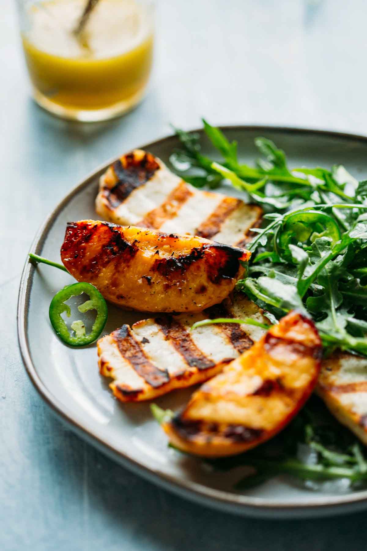 Grilled peaches and halloumi nestled on greens, served with jalapeño and honey vinaigrette in the background.