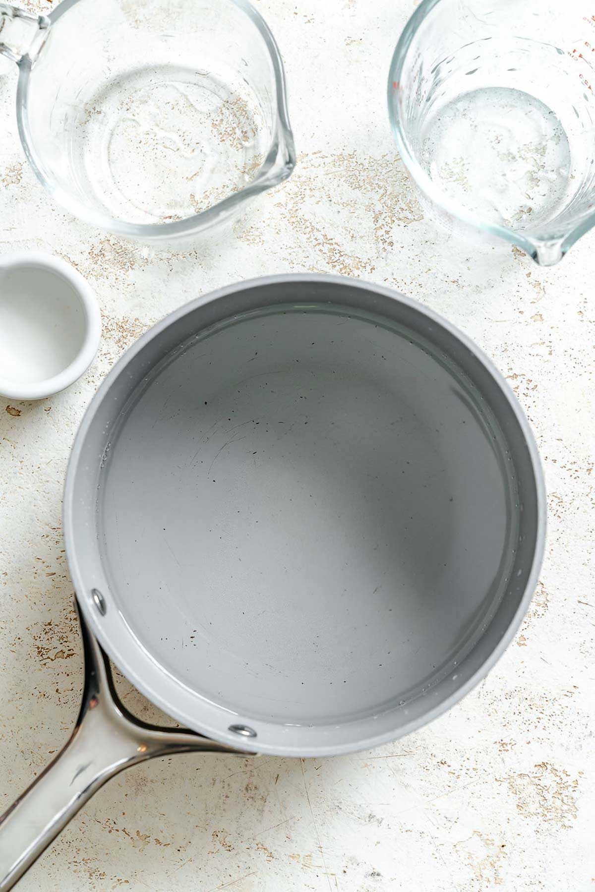 Overhead view of a pot of pickling liquid next to jars of vegetables – clear brine in a stainless pot alongside open jars of prepped giardiniera.
