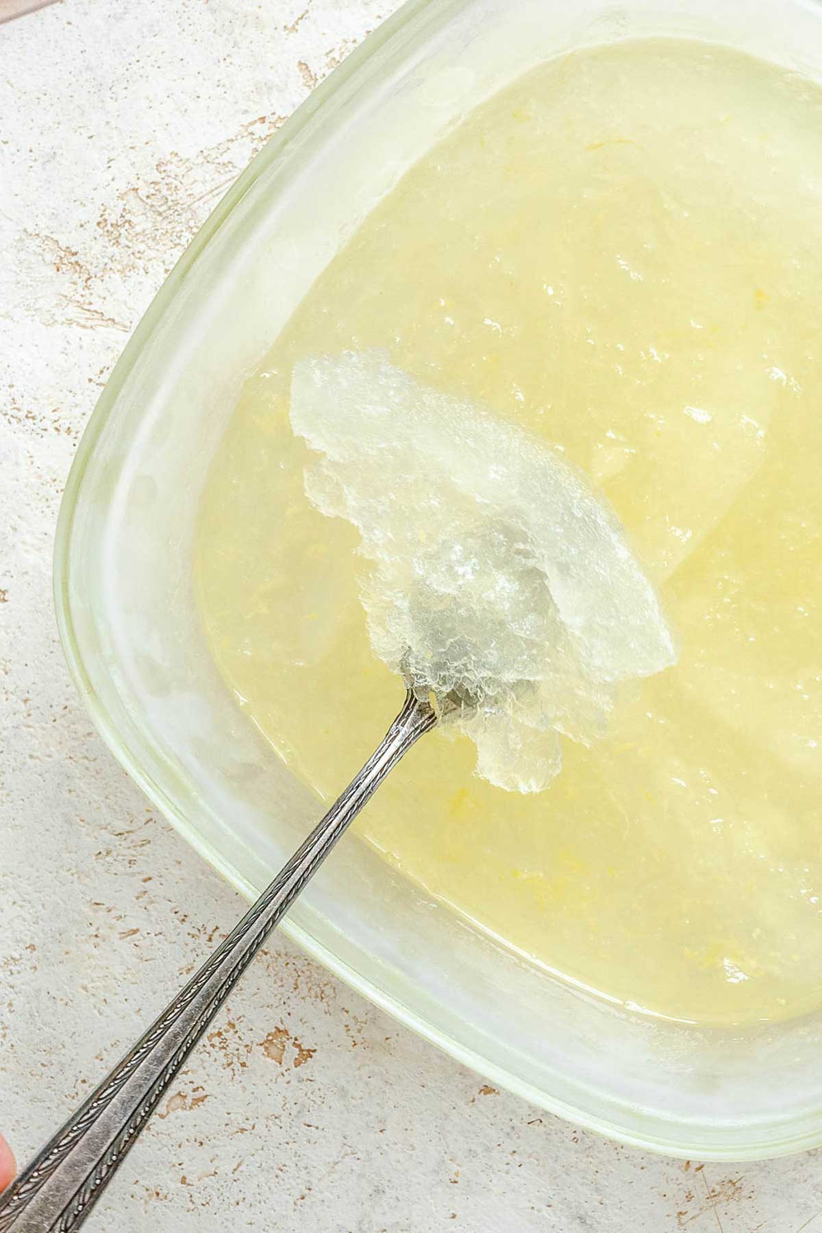 Close-up of icy shards of lemon granita in a glass container being scraped with a fork to form fine flakes.