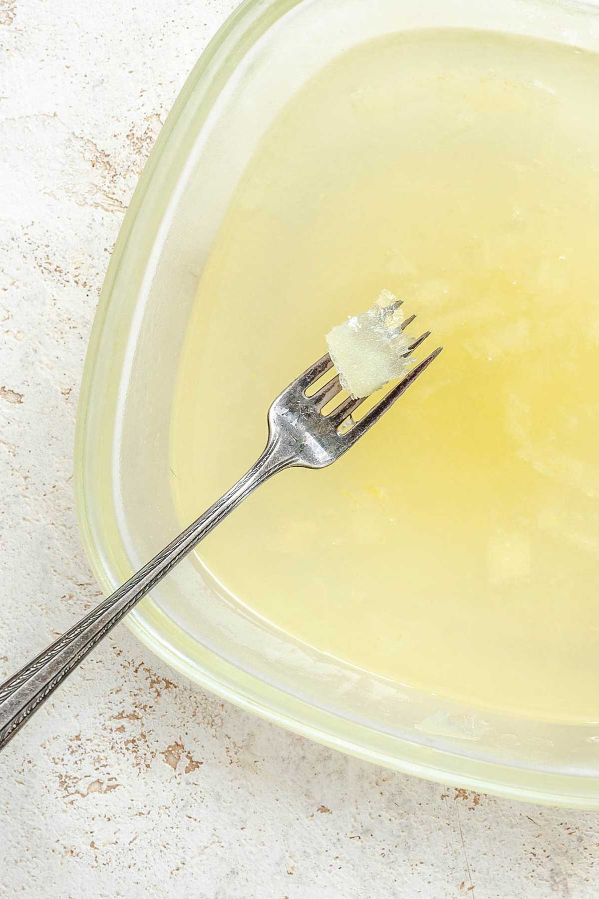A shallow dish of pale yellow lemon granita mid-freeze, with a fork scraping crystals from the surface.