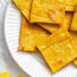Golden, square-cut chickpea fritters (panelle) sprinkled with flaky sea salt, arranged on a white ridged plate with lemon wedges on the side.