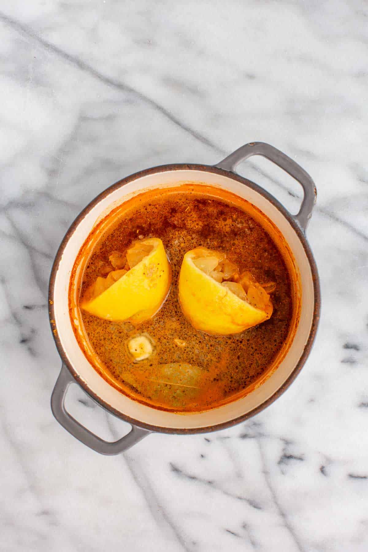 Overhead view of a Dutch oven with beer, Old Bay, lemon, garlic, and bay leaves simmering to make a flavorful shrimp boil broth.