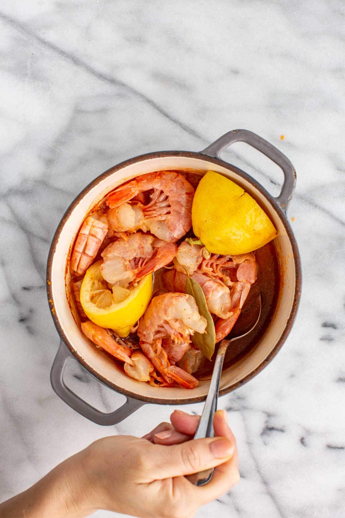 Shrimp simmering in the broth, turning pink as they cook alongside lemon halves and bay leaves.