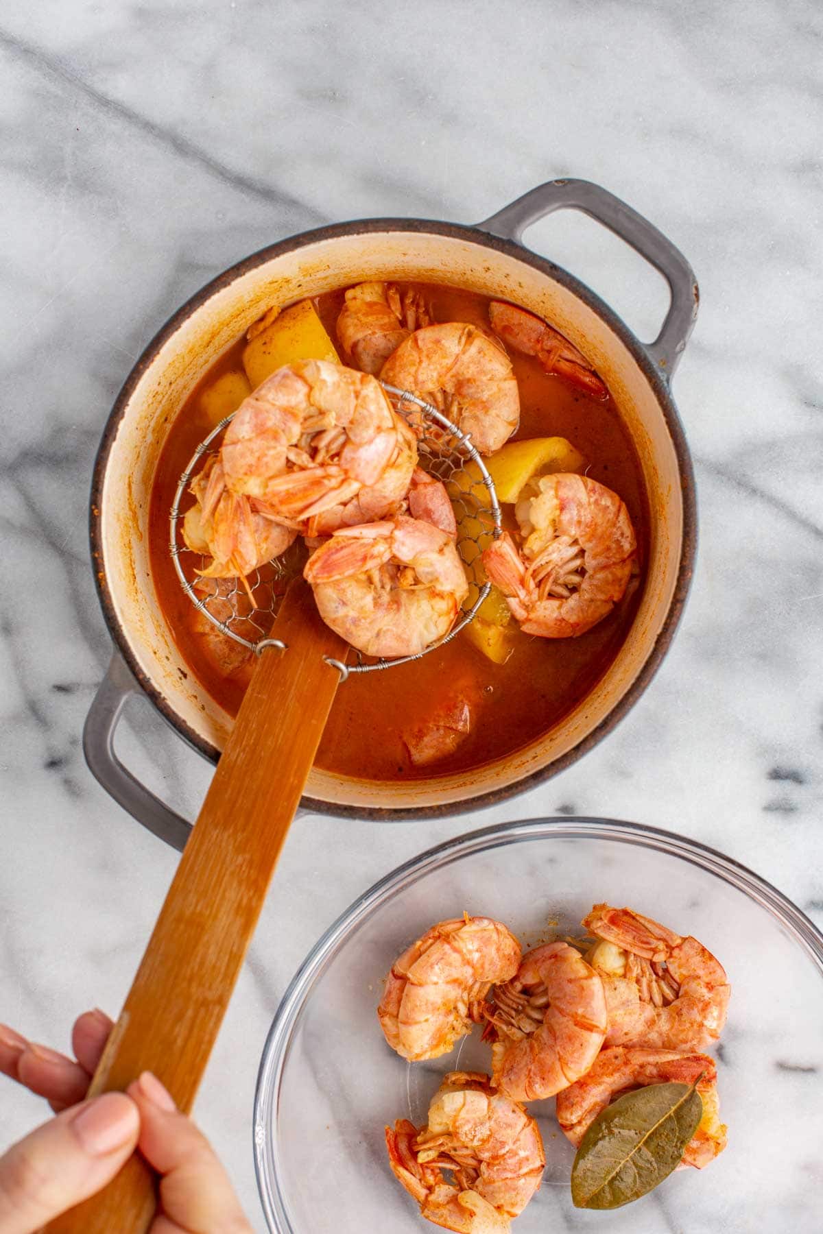 Cooked shrimp being lifted out of the pot with a slotted skimmer, ready to cool.