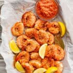 Spiced, cooked shrimp drained and cooling in a glass bowl with bay leaves and lemon wedges.