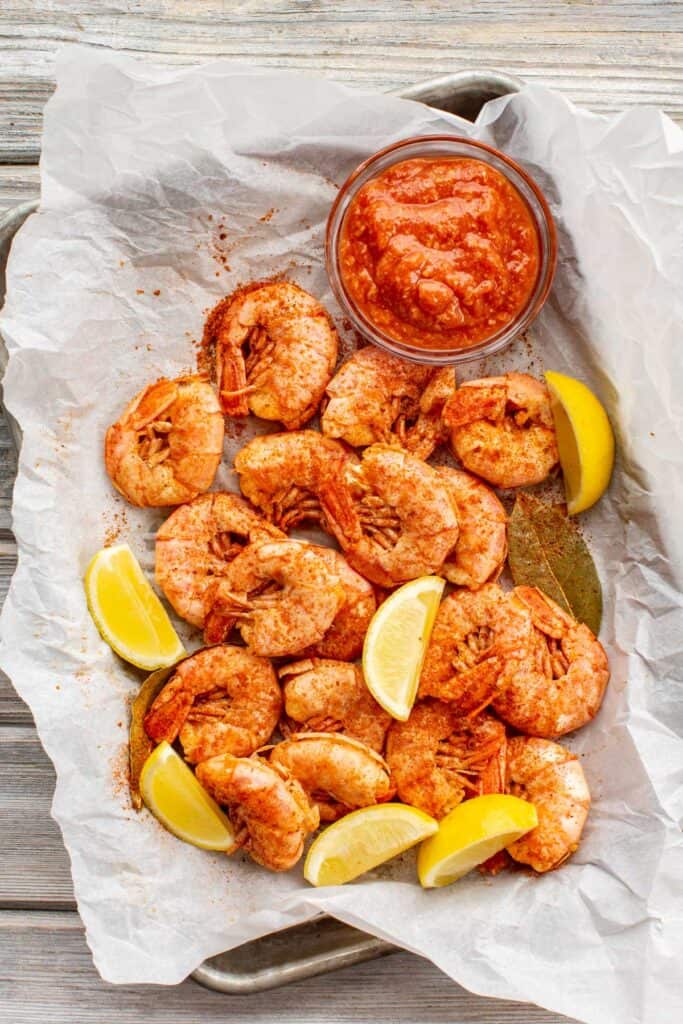 Spiced, cooked shrimp drained and cooling in a glass bowl with bay leaves and lemon wedges.