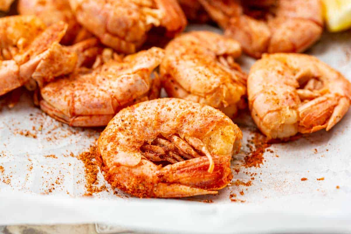 Serving tray lined with parchment paper, piled with seasoned shrimp, lemon wedges, and a bowl of cocktail sauce for dipping.