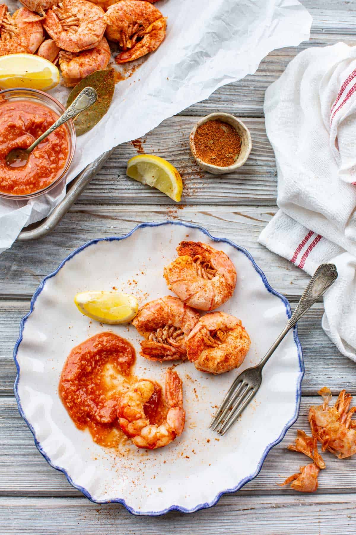 Peeled shrimp on a plate with cocktail sauce, shells scattered nearby, ready to be eaten.