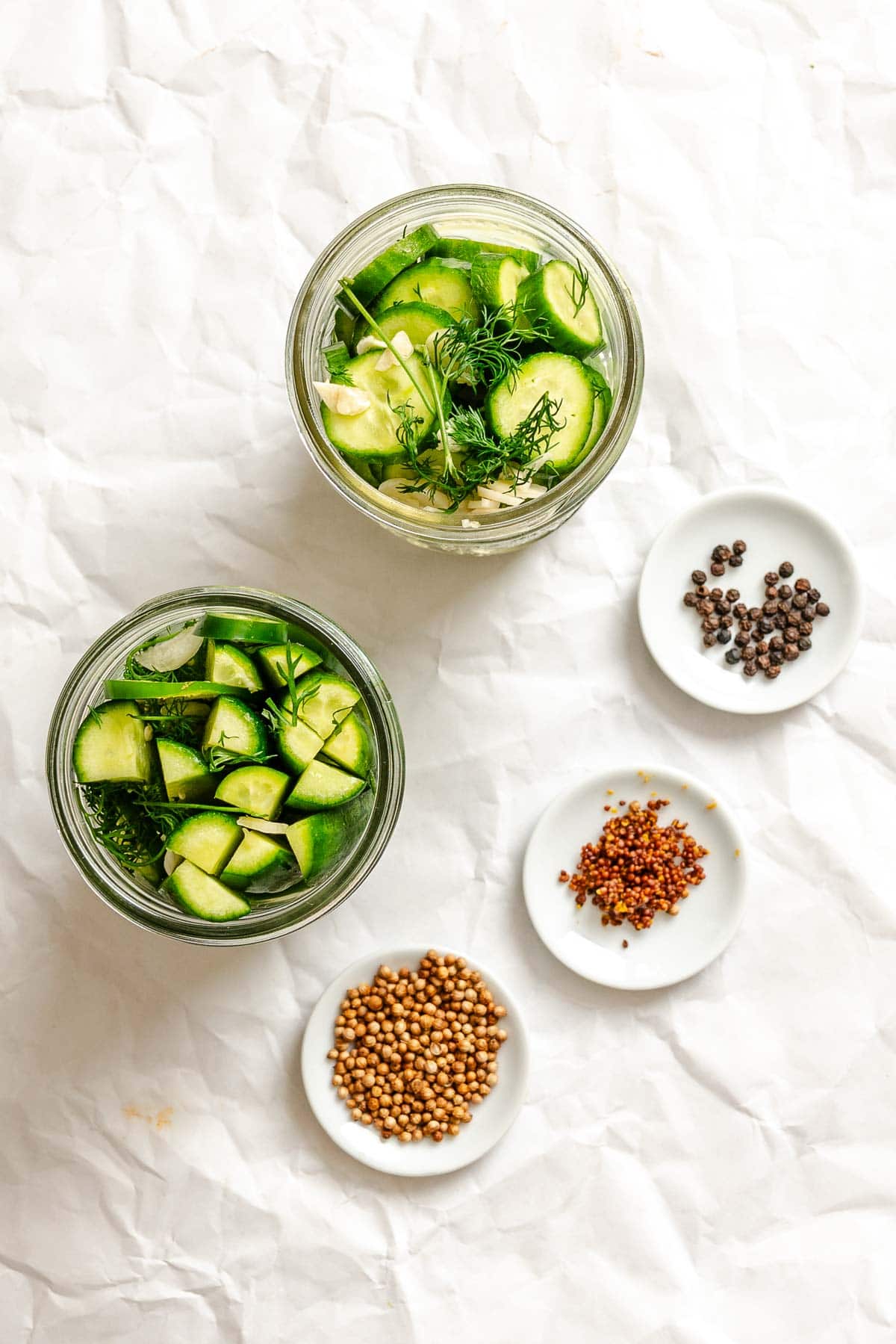 Glass jars filled with sliced cucumbers, garlic, dill, and pickling spices, ready for the brine to be added.