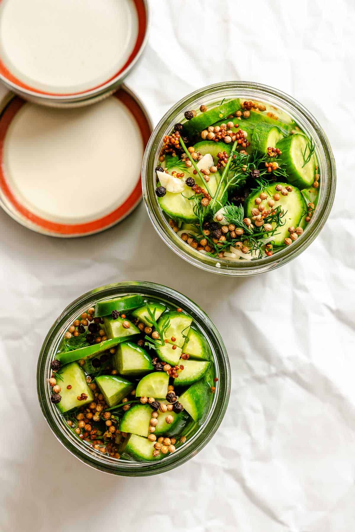 Close-up of a jar packed with cucumber slices, mustard seeds, peppercorns, garlic, and dill submerged in brine.