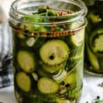View of a filled jar with chunky cucumber wedges, dill, garlic, and coriander seeds peeking through the liquid brine.