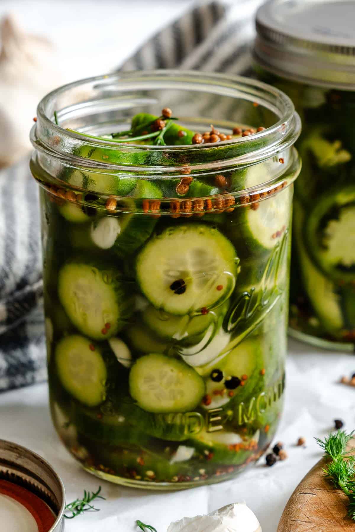 View of a filled jar with chunky cucumber wedges, dill, garlic, and coriander seeds peeking through the liquid brine.