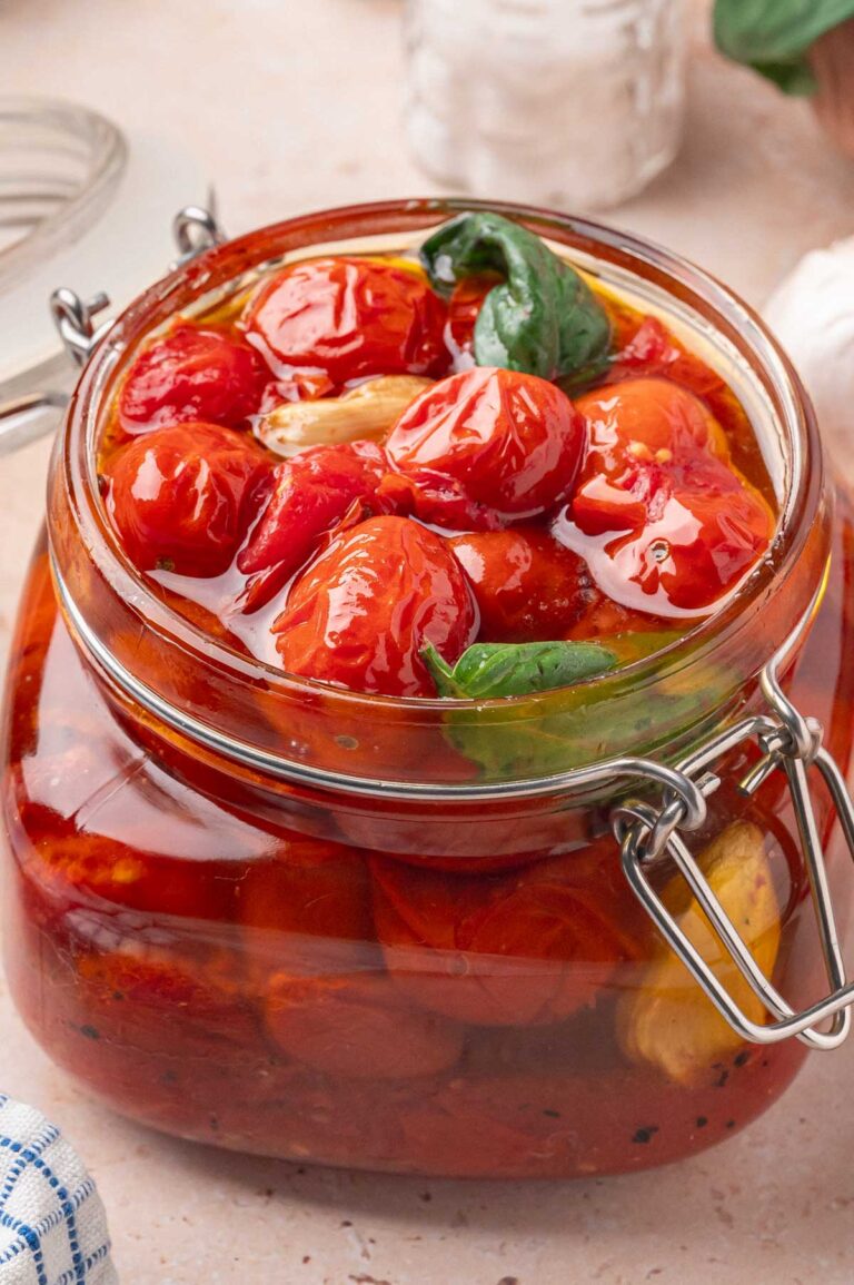 Zoomed-in view of cherry tomato confit packed in a glass jar with basil and oil.