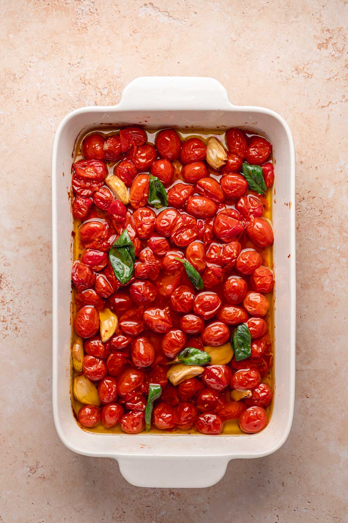 Roasted cherry tomatoes in oil, garnished with fresh basil leaves.