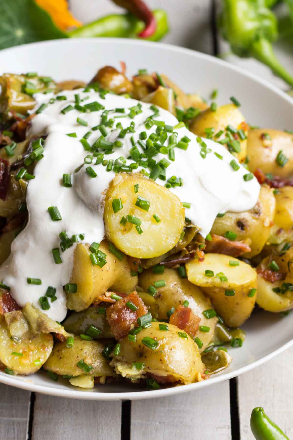 Angled close-up of potato salad with creamy sour cream and fresh chives on top, highlighting the sliced fingerling potatoes and crispy bacon bits.