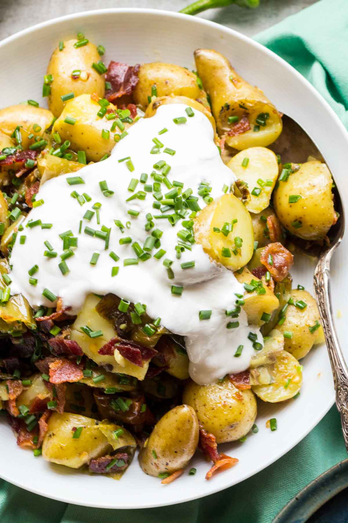 Bright, top-down shot of the plated salad with a large spoon, displaying the textures of the potatoes, herbs, and toppings.