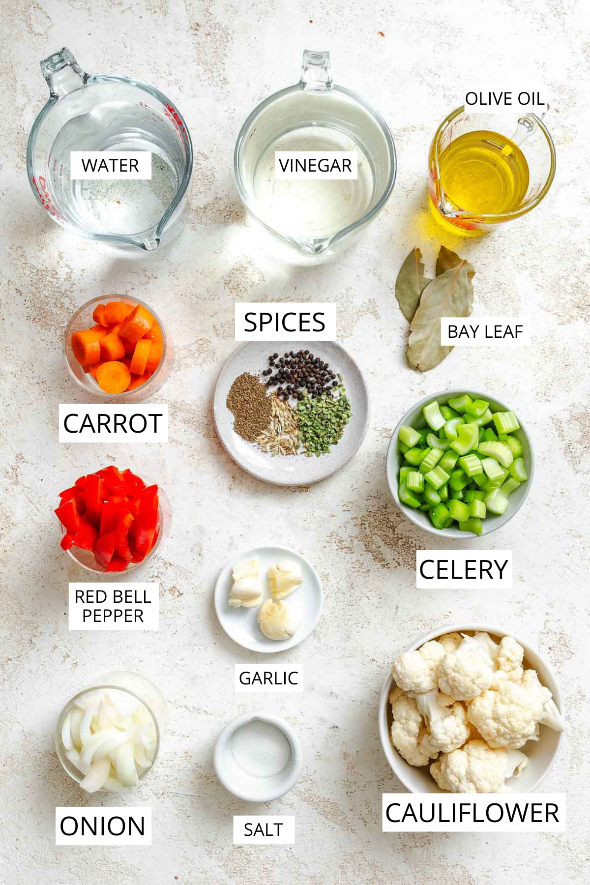 Flat lay of labeled ingredients for Italian giardiniera such as vinegar, carrot, spices, celery, garlic, cauliflower, onion and olive oil.